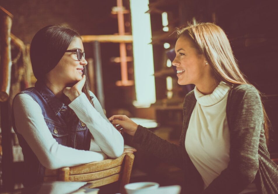Two,Young,Girls,Sitting,In,Cafe,And,Having,Conversation.